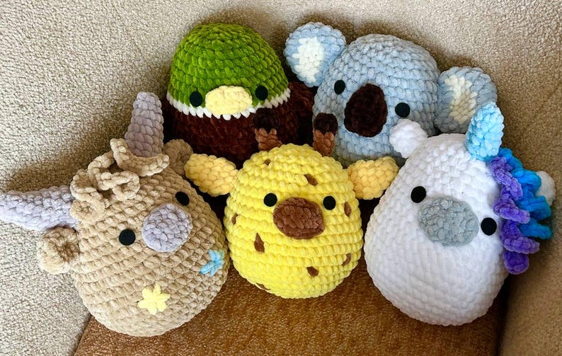 May include: Five handmade crochet animal plushies are shown. The collection includes a duck, koala, giraffe, unicorn, and a horned animal. Each plushie has a unique colour scheme and design, with black safety eyes.