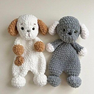 May include: Two handmade crochet dog stuffed animals. One is white with brown accents, the other is gray with white accents. Both have floppy ears, button eyes, and rounded paws. These plush toys are soft and cuddly.