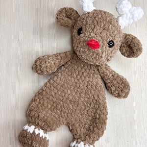 May include: A handmade brown crochet reindeer plush toy with white antlers and accents. The reindeer has a red nose, black eyes, and white details on its feet. This soft, cuddly toy is perfect for holiday decor or as a gift.