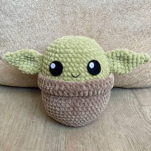 May include: A handmade plush toy in the likeness of a character from a popular science fiction series. The toy features a light green head with large black eyes, large ears, and a smiling mouth. The lower portion is a brown color.