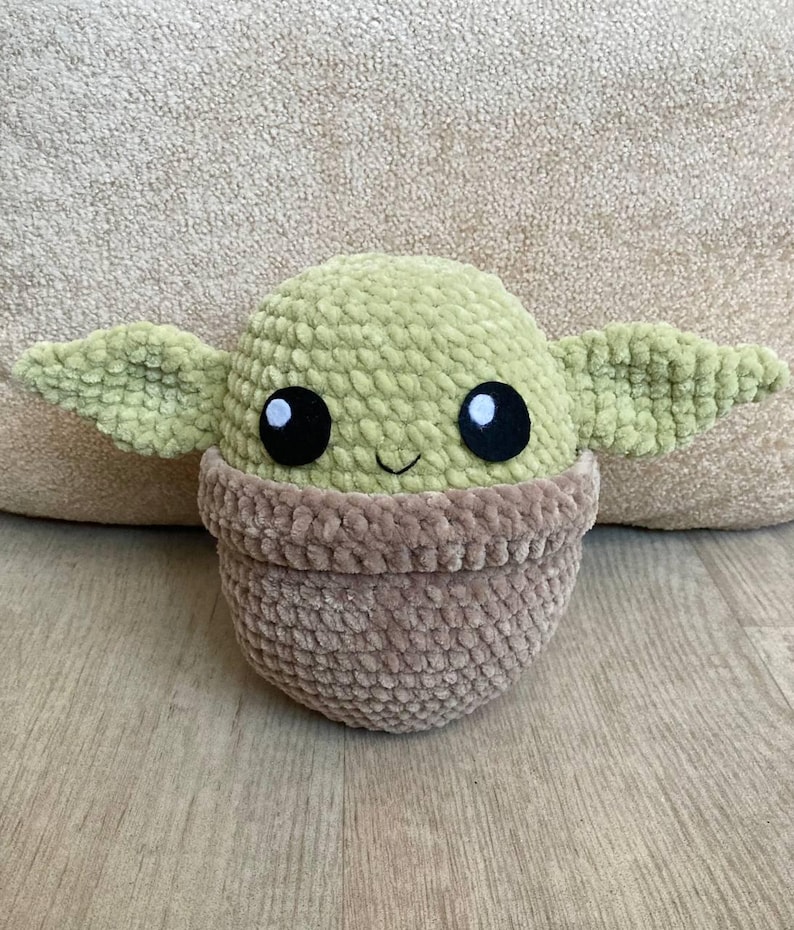 May include: A handmade plush toy in the likeness of a character from a popular science fiction series. The toy features a light green head with large black eyes, large ears, and a smiling mouth. The lower portion is a brown color.