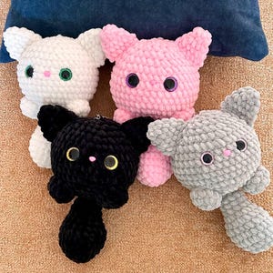 May include: Four handmade crochet cat plushies in white, pink, black, and gray. Each cat has large eyes and a small pink nose. The plushies are soft and cuddly, perfect for children or cat lovers.