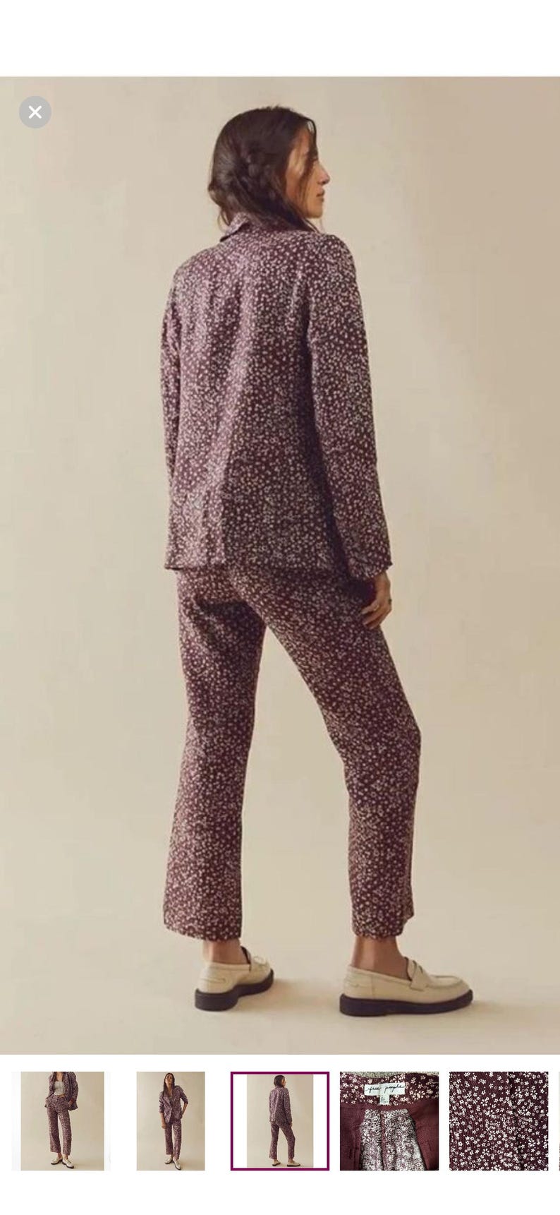May include: A two-piece floral pajama set in a burgundy color with small white flowers. The set includes a long-sleeved button-up shirt and matching pants. The model is wearing cream-colored loafers. The outfit is made of a soft, comfortable material.
