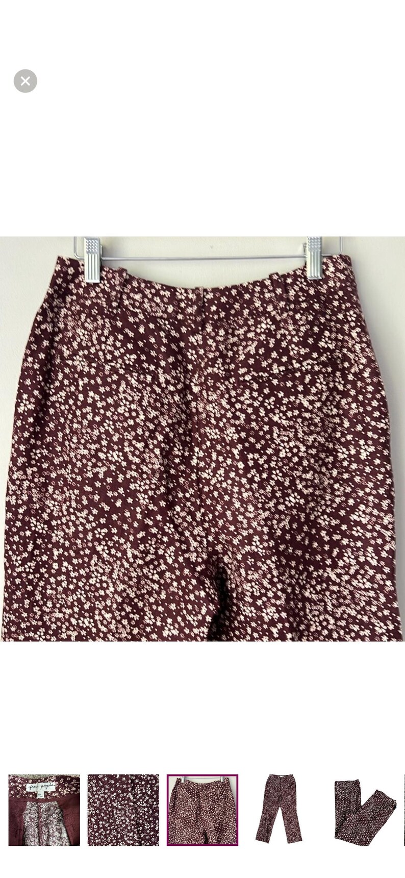 May include: Burgundy-colored pants with a white floral pattern, hanging on a silver hanger. The pants are made of a soft fabric and have a high waist. The floral pattern is small and evenly distributed across the fabric.
