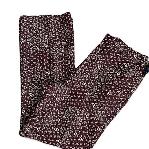 May include: Burgundy-colored pants with a white floral pattern. The pants are made of a lightweight fabric and have a straight leg cut. The floral print is evenly distributed across the fabric.