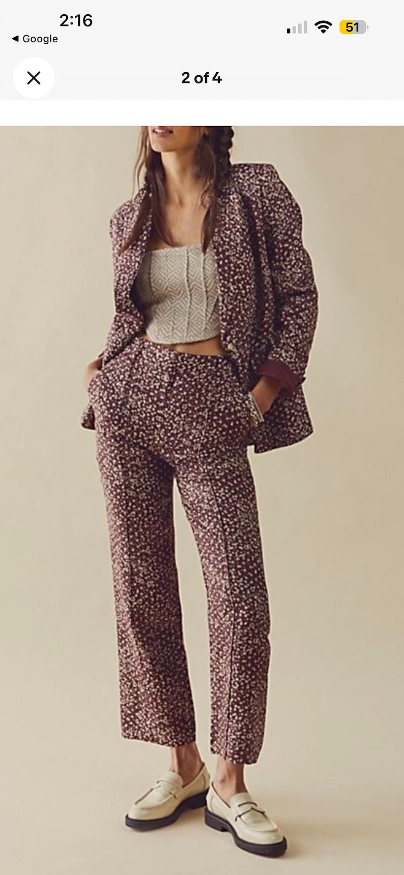 May include: A burgundy floral print suit, including a blazer and matching pants, paired with a cream-colored top and white loafers. The suit features a small, repeating floral pattern. The pants are straight-legged.