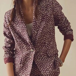 May include: A burgundy blazer and matching bottoms set with a white floral pattern. The blazer has a single button closure and the sleeves are cuffed. The outfit is a stylish ensemble for a variety of occasions.