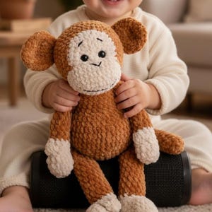 Puede incluir: Un juguete de peluche de mono hecho a mano en tonos marrón y crema. El mono tiene una cara sonriente, orejas grandes y está siendo sostenido por un niño. El juguete está hecho de un material suave y texturizado, y está diseñado para niños.