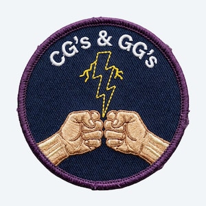 May include: A circular embroidered patch with a dark blue background and a purple stitched border. The design features two tan fists bumping together, a yellow lightning bolt above them, and the white text CG's & GG's arched at the top.