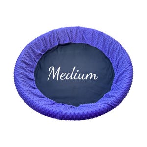 May include: A medium-sized pet bed with a plush, textured purple exterior and a dark blue interior. The word "Medium" is written in white script across the center of the bed.