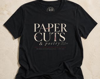 May include: A black short-sleeve t-shirt featuring the cream-colored text PAPER CUTS & poetry with red accents. Below the main text, it reads that one was personal, INK STAINED HEARTWEAR CLUB, and THE PROSE & STITCH COLLECTIVE EST. 2024.