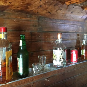 May include: A wooden shelf with a variety of bottles and a can. The bottles include a clear bottle with a red cap, a green glass bottle, a clear bottle with a cork top, a clear bottle with a brown cap, and a clear bottle with a red cap. The can is red and white and has the word "Coca-Cola" on it.