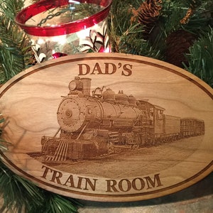 May include: A wooden oval sign with the text "DAD'S TRAIN ROOM" and a laser-engraved image of a vintage steam locomotive.