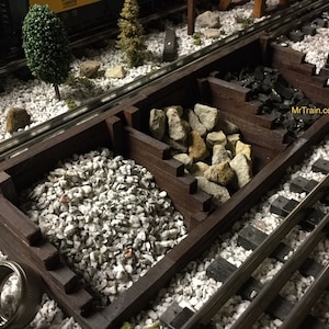 May include: A wooden model train hopper with three compartments. The compartments are filled with white gravel, tan rocks, and black coal. The hopper is sitting on a model train track.