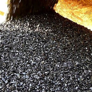 May include: A large pile of black gravel being poured from a chute. The gravel is a dark, almost black color and is piled high.