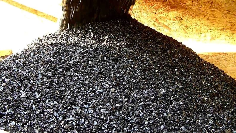 May include: A large pile of black gravel being poured from a chute. The gravel is a dark, almost black color and is piled high.
