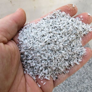 May include: A close-up of a handful of small, white and gray gravel. The gravel is about the size of a grain of rice.