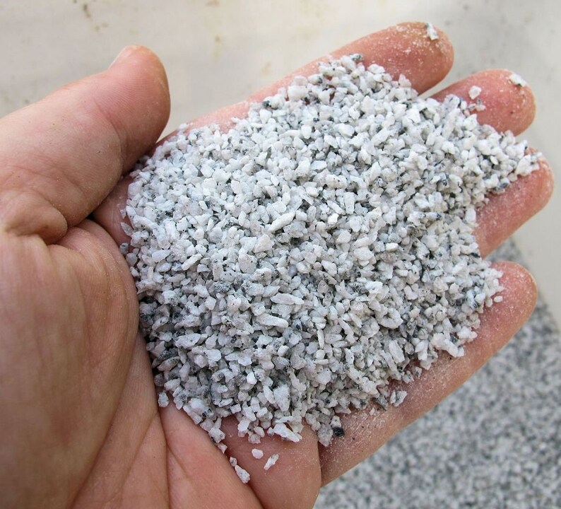 May include: A close-up of a handful of small, white and gray gravel. The gravel is about the size of a grain of rice.