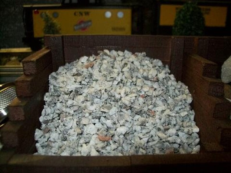 May include: A close-up of a wooden box filled with gray gravel. The gravel is a mix of small and large stones.