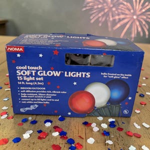 May include: A blue box of NOMA Soft Glow Lights, 15 light set, 14 ft. long. The box features red, white, and blue bulbs, with the text "cool touch SOFT GLOW LIGHTS." The bulbs are 50mm in diameter and fade-resistant.
