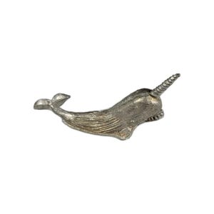May include: A silver-colored narwhal figurine with a spiraled tusk. The whale has detailed fins and a textured body. The figurine is a decorative item, likely for display.