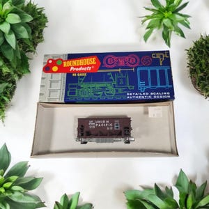 May include: A model train car in a box. The box is blue with the words "Roundhouse Products" and "HO Gauge". The train car is brown with the words "UP UNION PACIFIC" printed on the side. The box is open.