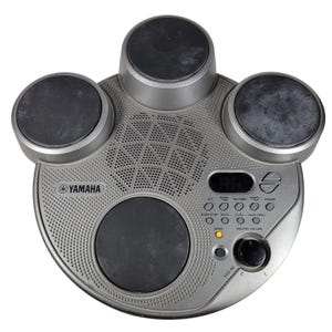 Puede incluir: Batería electrónica Yamaha YDD-40 plateada con cuatro pads de batería negros. El kit tiene un altavoz, un panel de control y una pantalla digital. El logotipo de Yamaha es visible.