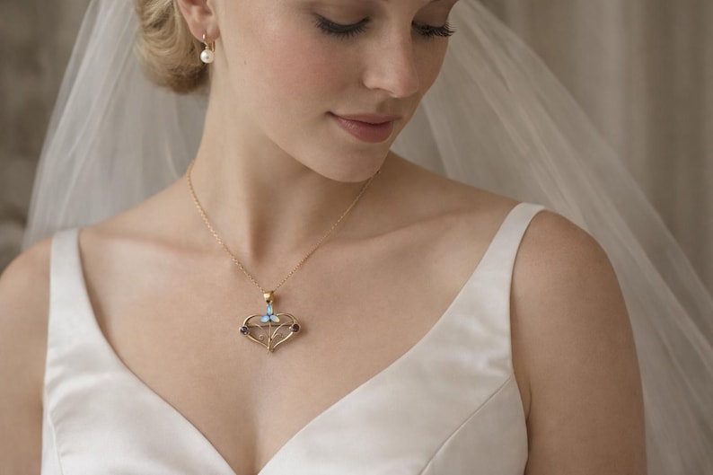 May include: A gold necklace with a heart-shaped pendant featuring a light blue butterfly and two dark red gems. The necklace is worn by a person wearing a white dress and veil, with a pearl earring.