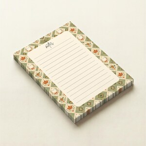 May include: A rectangular notepad with a cream-colored writing area featuring horizontal lines and the word notes printed in black. The border displays a repeating diamond pattern in shades of green, orange, and white, decorated with autumn leaves and acorns.