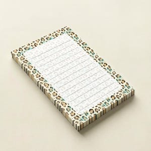 May include: A rectangular notepad featuring a white interior with horizontal lines for writing. The border of the notepad is decorated with a repeating leopard print pattern in shades of brown, tan, and teal, which also extends to the side edges.