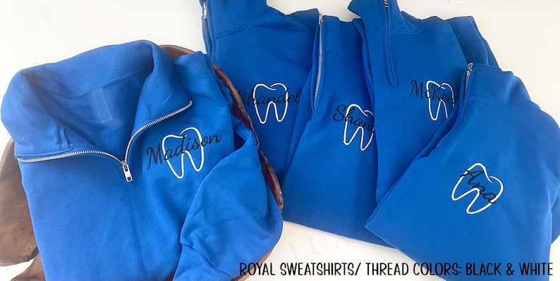 Puede incluir: Sudaderas azul real con cremallera de cuarto de cremallera y bordados blancos de dientes y nombres. Las sudaderas tienen una cremallera plateada y se muestran sobre una superficie blanca. El texto "ROYAL SWEATSHIRTS/ THREAD COLORS: BLACK & WHITE" est&aacute; en la parte inferior.