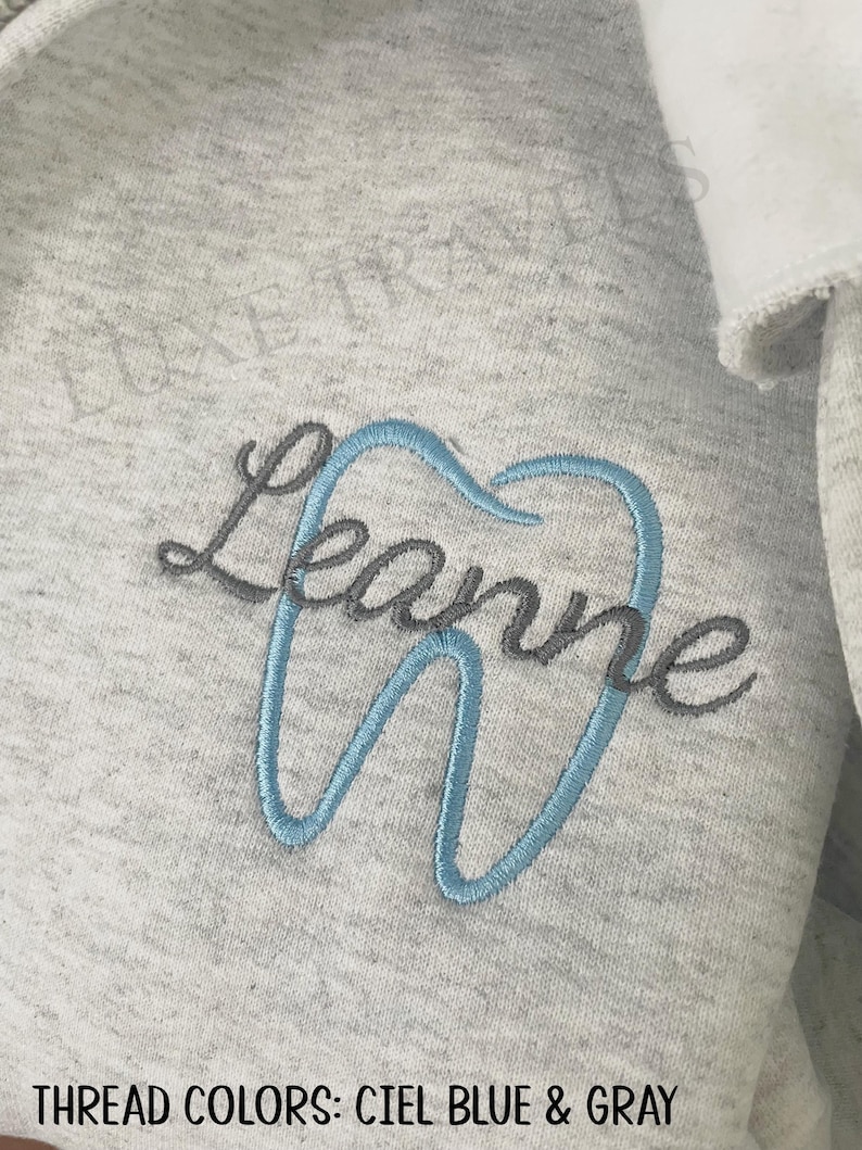 Puede incluir: Sudadera gris claro con un dise&ntilde;o bordado. El dise&ntilde;o presenta el nombre "Leanne" en escritura gris, con la letra "e" formando el contorno de un diente en azul claro. El texto "THREAD COLORS: CIEL BLUE & GRAY" est&aacute; en la parte inferior.