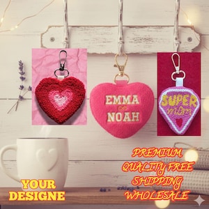 May include: Three heart-shaped keychains. One is red with a lighter red and white center. Another is pink with "EMMA & NOAH" embroidered in white. The third is a pink diamond shape with "SUPER MOM" in yellow.