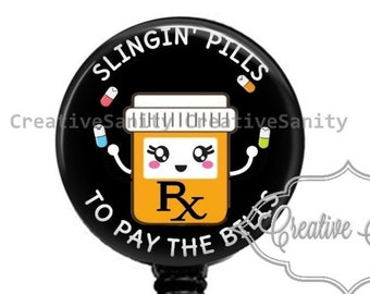May include: Black and white badge reel with a black button and a clear plastic clip. The badge reel features a cartoon pill bottle with a smiling face and the text "SLINGIN' PILLS TO PAY THE BILLS".
