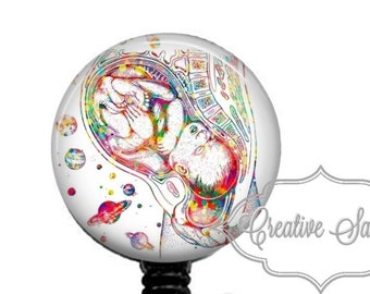 May include: A colorful anatomical illustration of a baby in utero, printed on a round badge holder with a black retractable cord and a clear plastic clip.