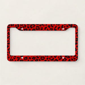 May include: A red license plate frame with a black leopard print pattern. The frame has a rectangular shape with rounded corners and four mounting holes. The leopard spots are irregularly shaped and distributed across the frame.