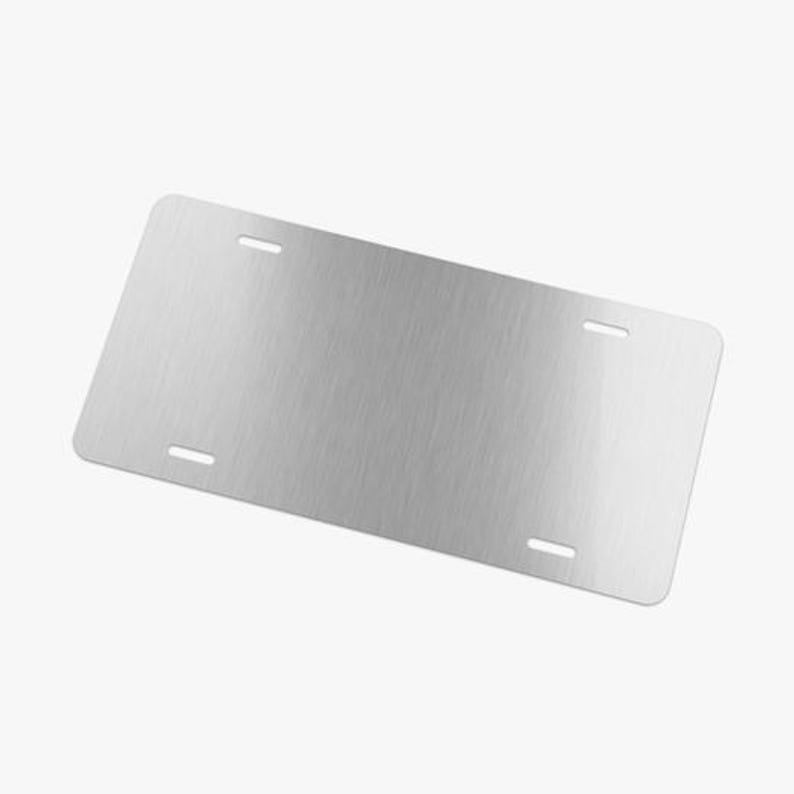 May include: A blank, brushed metal license plate with four oblong mounting holes. The plate has rounded corners and a silver finish. The surface has a subtle, horizontal grain.