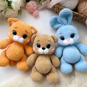 Può includere: Tre animali di peluche realizzati all'uncinetto a mano, tra cui un gatto arancione, un orso beige e un coniglio azzurro. Ogni giocattolo presenta grandi occhi scuri, un muso bianco e piccoli dettagli rosa sulle guance, creati con filato morbido.