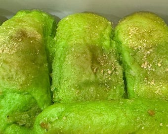 May include: Close-up of several green, oblong-shaped pastries. The pastries have a vibrant green hue with a slightly textured surface and are dusted with a light-colored powder. The image suggests a bakery or food-related theme.