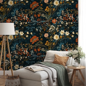 May include: A dark floral wallpaper featuring a dense pattern of orange, white, and yellow flowers with green and blue foliage. The wallpaper is the backdrop for a white chaise lounge with pillows, a side table, and a floor lamp.