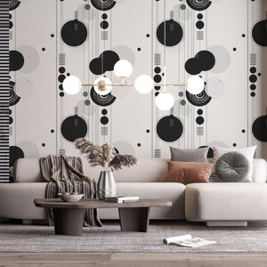 May include: A modern living room with a beige sectional sofa, a dark wood coffee table, and a patterned rug. The wall features a black and white geometric wallpaper. A gold chandelier with white globe lights hangs above.