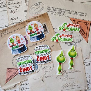 May include: A collection of seven die-cut stickers featuring green Grinch characters and Cindy Lou Who. Designs include snow globes with the text MERRY GRINCHMAS, script text reading MERRY GRINCHMAS, and rectangular shapes with the text IN A WORLD FULL OF GRINCHES BE A CINDY LOU WHO.