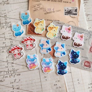 May include: A collection of colorful cat-shaped stickers with various designs, including cats with star, mushroom, and ice cream cone motifs. The stickers are on a vintage paper background with French text and stamps.