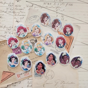 May include: A collection of fifteen oval-shaped flatback cabochons featuring illustrations of various animated princesses. Each piece displays a unique character portrait framed by a decorative white border with small floral or crown-like details.
