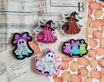 Puede incluir: Cinco dijes de acrílico con forma de fantasma y bordes brillantes. Un fantasma tiene un lazo rosa, otro es rosa con sombrero de bruja y calabaza, otro tiene estampado de leopardo naranja, otro es floral y otro muestra tres pequeños fantasmas.