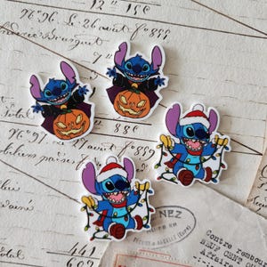 May include: Four die-cut stickers featuring the blue alien character Stitch. Two stickers show Stitch wearing a black cape and holding a carved jack-o'-lantern. Two stickers show Stitch wearing a red Santa hat and holding a string of colorful holiday lights.