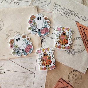 Puede incluir: Cuatro pegatinas troqueladas con ilustraciones de fantasmas. Dos pegatinas muestran un fantasma blanco rodeado de flores coloridas. Dos pegatinas muestran un fantasma con estampado floral haciendo el signo de la paz, con el texto "hippie halloween".