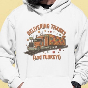 May include: White hoodie featuring an orange semi-truck graphic with the text "DELIVERING THANKS (and TURKEY!)". The truck's trailer is decorated with fall leaves. The design includes falling leaves and a small turkey.