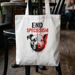Könnte beinhalten: Eine weiße Stofftasche mit einem grafischen Druck eines geteilten Tiergesichts, halb Hund und halb Schwein, mit roten und schwarzen Tintenspritzern. Der Text END SPECIESISM ist in fetten schwarzen und roten Buchstaben über der Illustration gedruckt.