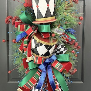 May include: A decorative Christmas swag featuring a top hat and drum with black and white diamond patterns, accented by red, green, and blue ribbons, pine needles, glittery red berries, and blue bead sprays, finished with two black boots with white fur trim.